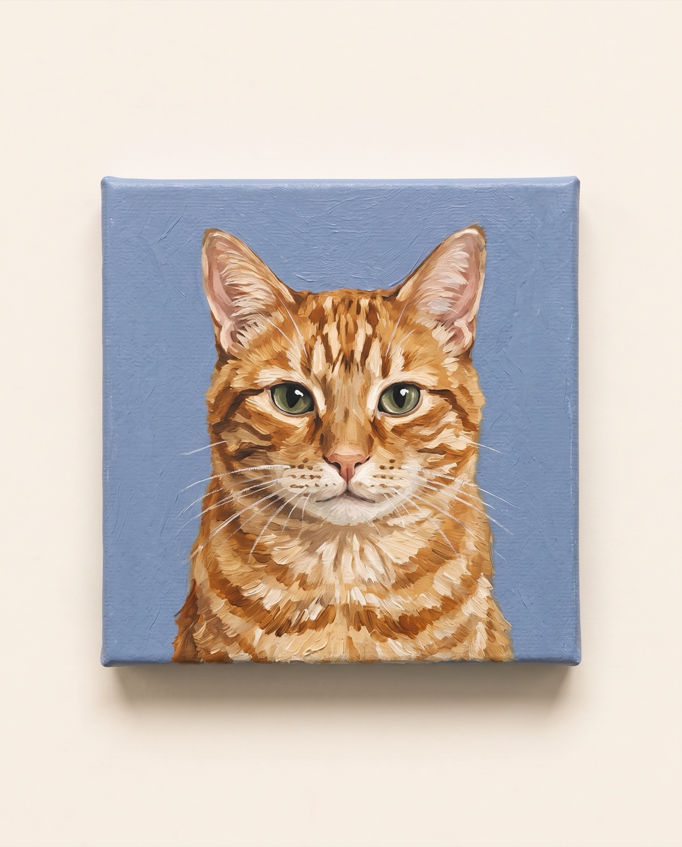 Acrylic painting of an orange tabby cat with green eyes on a small square canvas, photographed on cream paper